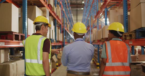 Diverse male and female workers wearing safety suits and talking in warehouse