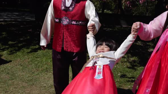 Korean Family in National Costumes in Nature Stands Next to a Cherry Blossoming Tree