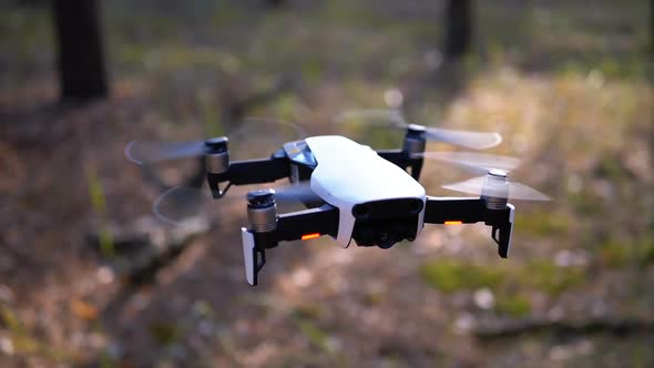 Drone with a Camera Hovers in the Air Above the Ground in the Forest