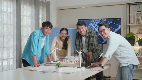 Asian Engineers Group Smiling To Camera While Working About Small House Model With Solar Panel