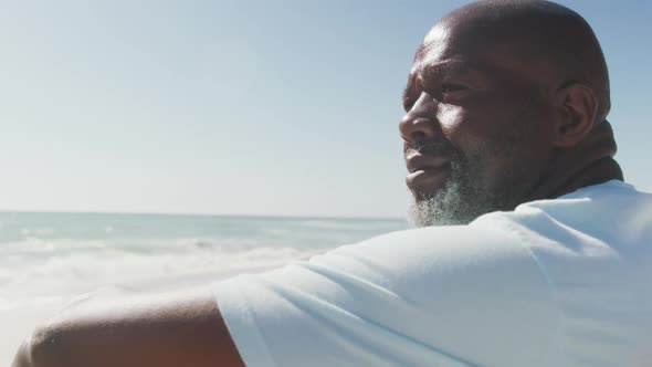 Senior african american man wearing white tshirt sitting on sunny beach