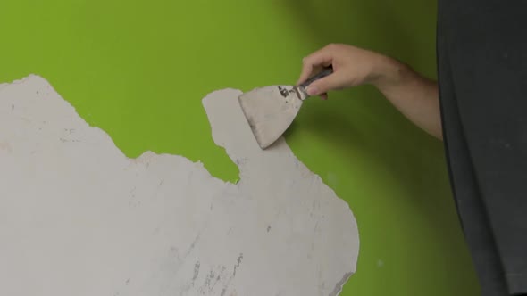 steady wide shot of a man scraping off green paint from a wall
