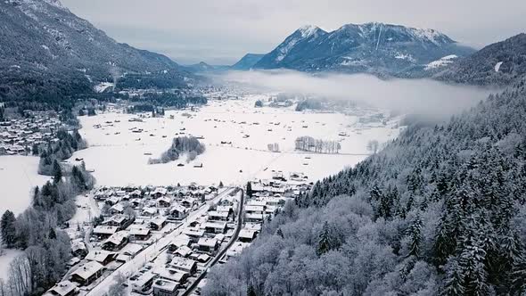 Aerial shot of snowy landscape in Grainau towards the Zugspitze mountain and a cloud, in Bavaria, Ge