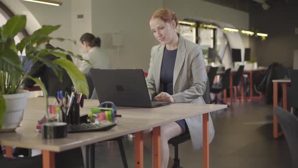 Portrait of Confident Caucasian Redhead Woman Working in the Office Using Laptop. Young Female