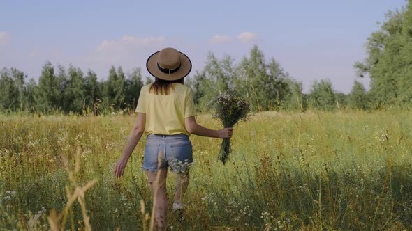 Happy Woman with Bouquet of Wildflowers Walking and Picking Flowers in Meadow Back View