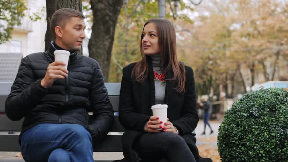 Happy Couple with Paper Glasses in Hands Talking on City Bench on the Street