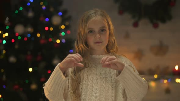 Cute Girl Making Heart With Hands Looking to Camera, X-Mas Tree Glowing Behind