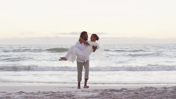 African american couple in love getting married, man carrying woman on the beach at sunset