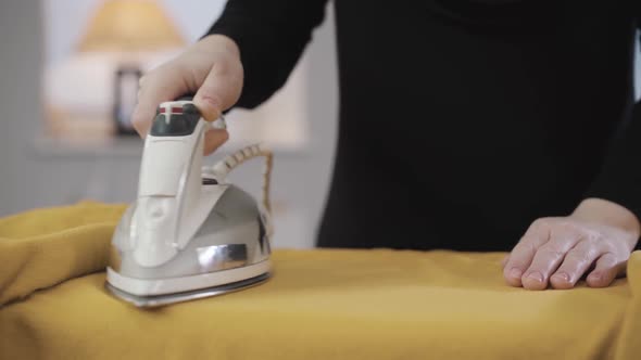 Close-up of Female Hands Ironing Yellow Sweater. Young Muslim Housewife Doing Housework. Eastern