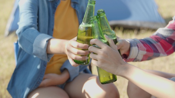 Asian woman happy with friends camping in nature having fun together drinking beer.