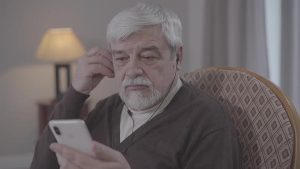 Close-up of Mature Caucasian Man Putting on Earphones and Turning on Music on Smartphone. Positive