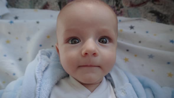 Funny Child Lies in Bed Looks at the Camera and Shows Different Emotions