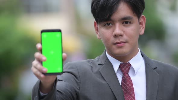 Young Handsome Asian Businessman Showing Phone in the Streets Outdoors