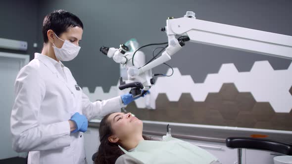 Female Dentist Examining Patients Teeth with Microscope