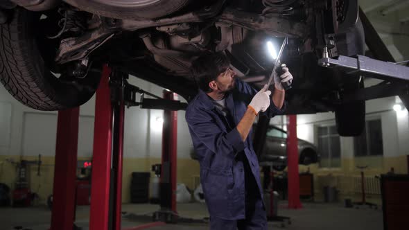 Auto Mechanic Checking Chassis of Car on Lift