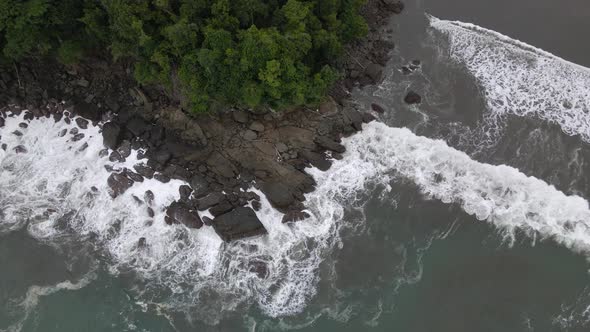 Top down aerial shot of strong sea waves crashing against rocks on the coast