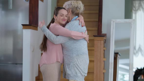 Side View Portrait of Happy Smiling Senior and Young Women Hugging and Talking Standing at Home
