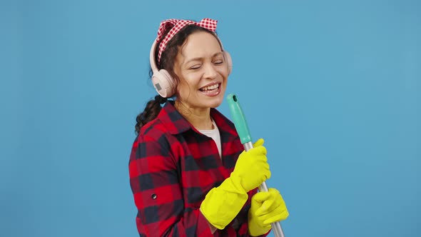 Happy Housewife Enjoying Home Cleaning Listening to Music in Wireless Headphones and Singing Into