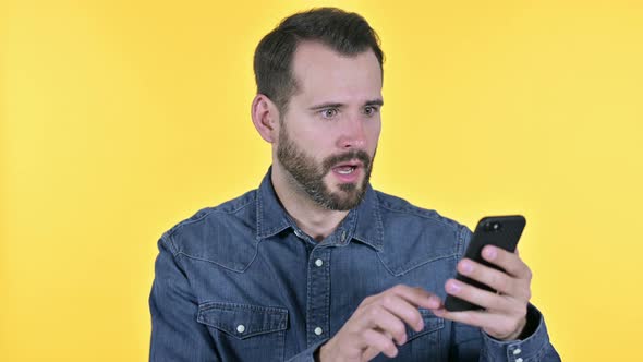 Beard Young Man Getting Shock on Smartphone, Yellow Background