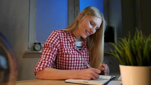 Cheerful Female Writing in Daily Planner. Lively Young Blond Woman in Casual Checkered Shirt Sitting