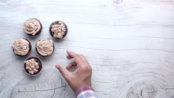 Man's Hand Picking Chocolate Cup Cake From Wooden Table.