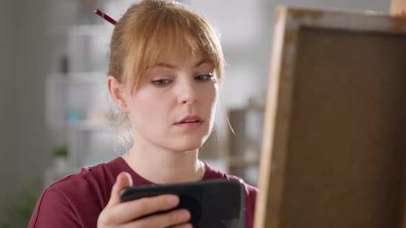 Young Attractive Woman Learns to Draw Using Video Lesson on Mobile Phone