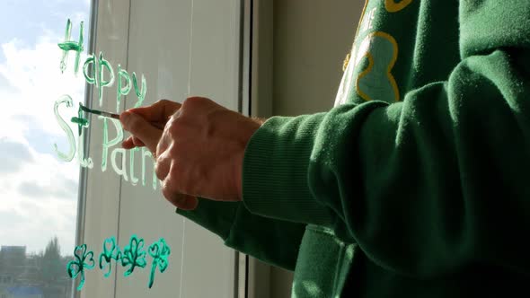 Drawing St. Patrick's Day Man painting green three-leaved shamrocks indoor Сlover leaves on window