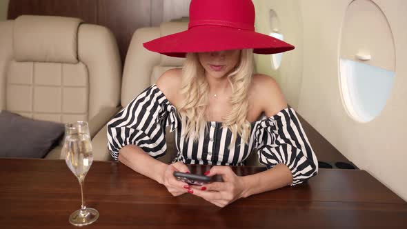 Portrait of a Blonde with Big Breasts a Red Hat and a Striped Dress on Board a Private Plane