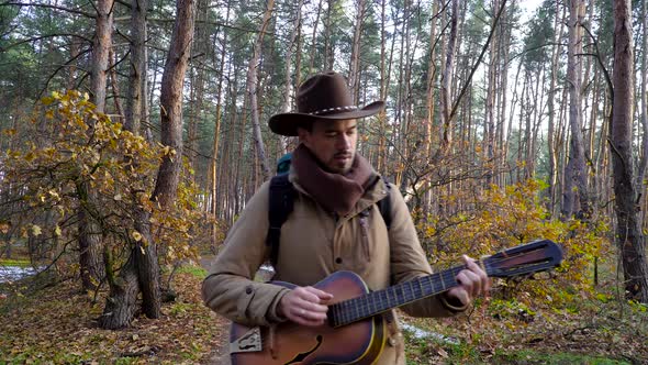 A Backpacker with a Guitar Walks Along a Trail in the Forest