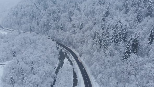 Aerial shot: cars and trucks are driving by the road in winter forest.