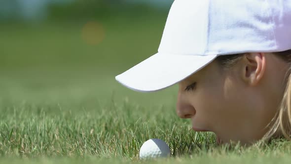 Woman Golf Beginner Player Lying on Grass and Blowing Ball Into Hole, Having Fun