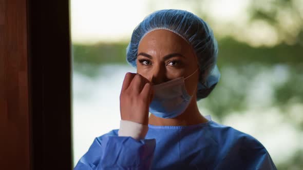 Close View of Young Female Doctor or Nurse Taking Off Surgical Face Mask and Looking at Camera