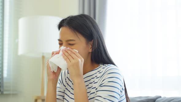 Asian beautiful woman having running nose and sneezing in living room.