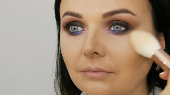 Close Up View of a Stylist Makeup Artist Applies Foundation Cream with a Special Brush on the Face