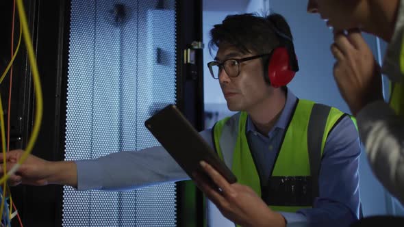 Diverse female and male it technicians wearing headphones using tablet checking computer server