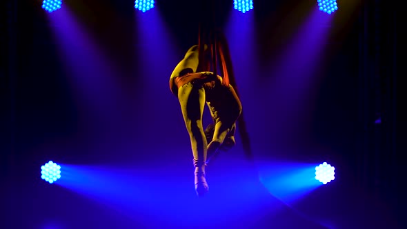 Young Woman Doing Show Acrobatic Trick on Air Silk. Exciting Acrobatic Show in a Dark Studio