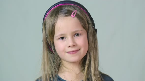 Pretty Smiling Cild Girl Listening to Music in Big Pink Earphones