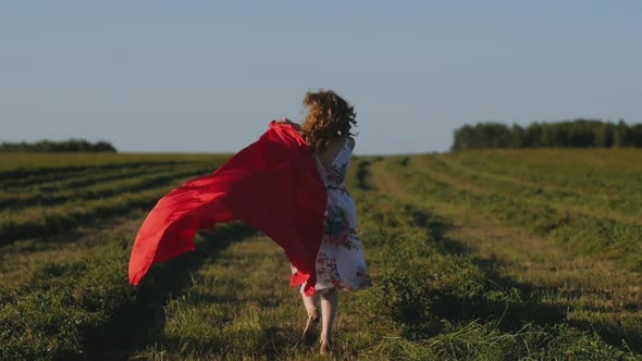 Redhead Woman in White Dress with Red Cloth in Her Hands on Background of Field