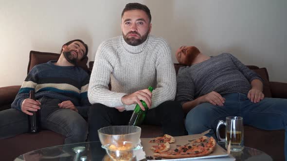 Young Bored Man Drinking Beer From Bottle Siting on Couch Watching Using TV