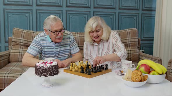 Retired Senior Couple Talking Drinking Tea Playing Chess in Modern Living Home Room Lounge Together