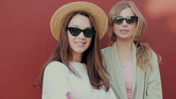 Two young beautiful smiling hipster girls in trendy white sweater and coat posing outdoors