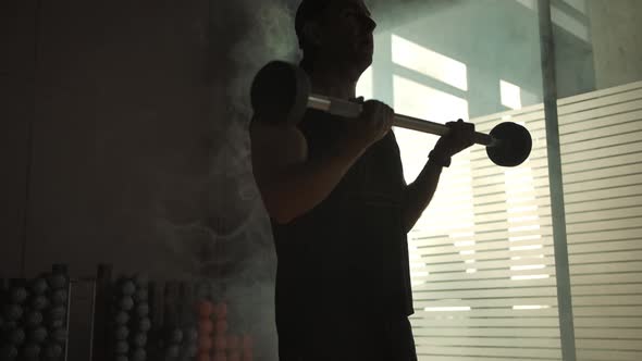 The Silhouette of an Adult Male Lifting a Barbell for Biceps Pumping Up