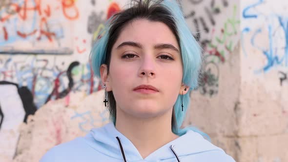 Blue haired teenage girl in hoodie screaming with hands near head. Head portrait against graffiti