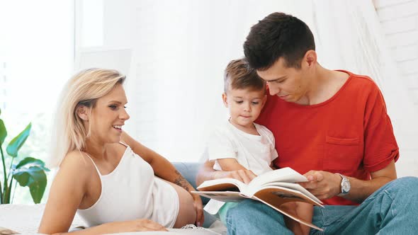 Happy Family  Pregnant Mother Father and Little Son Reading a Book at Home Family Concept