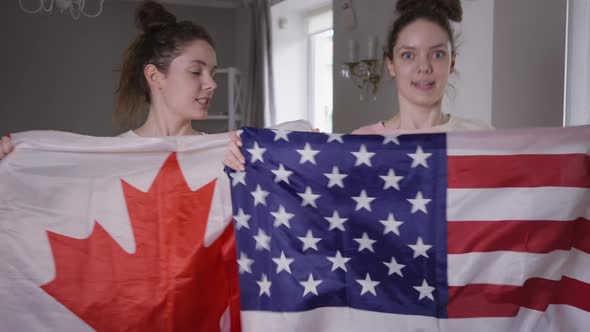 Twin Sisters with Canadian and US Flags Watching Championship on TV at Home Supporting Hockey or