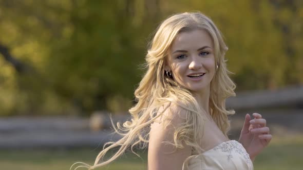 Woman with Blond Hair Stands with Her Back To Camera, Then Turns, Her Hair Is Fluttering in Sunny