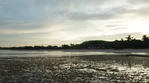 Low tide in tropical bay with silhouette shore from rising sun behind it, drone