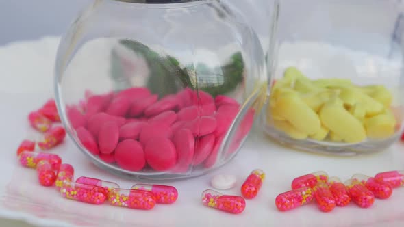 Rotating shot of pink and yellow tablets in a glass bottle with granule capsule around