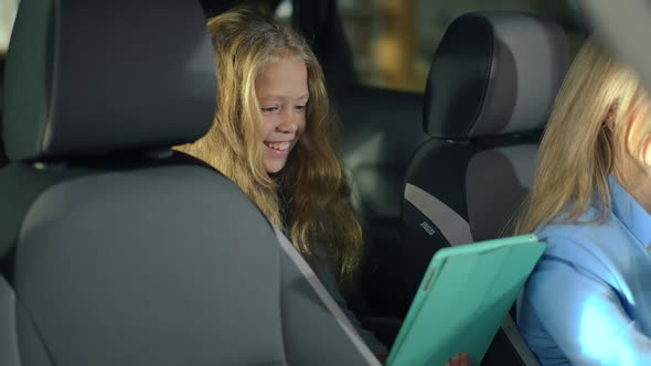 Pretty Smiling Caucasian Girl with Tablet Sitting in Car with Unrecognizable Woman Choosing New