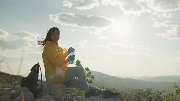 A Girl Drinks Water Sitting on a Stone in the Mountains